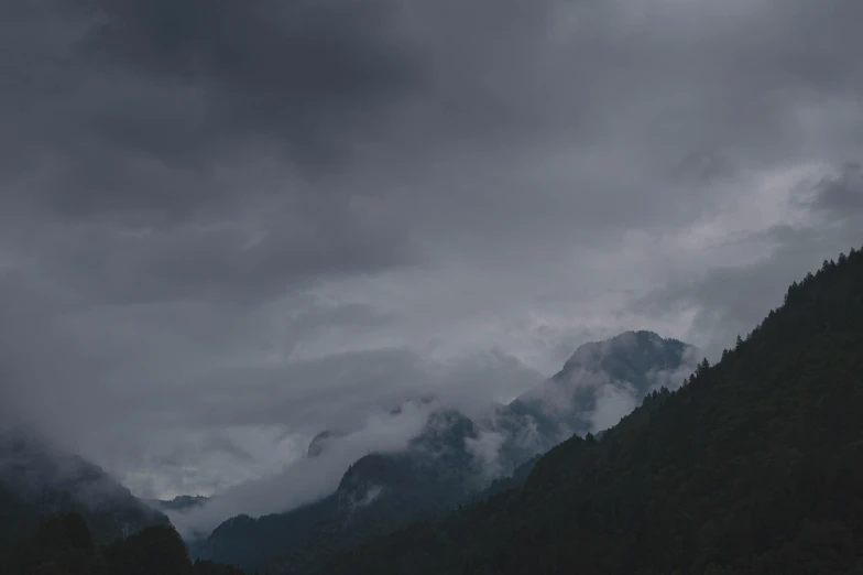 a dark landscape with trees and clouds in the background