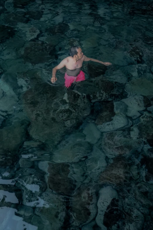 a man in pink swim trunks wading through shallow water