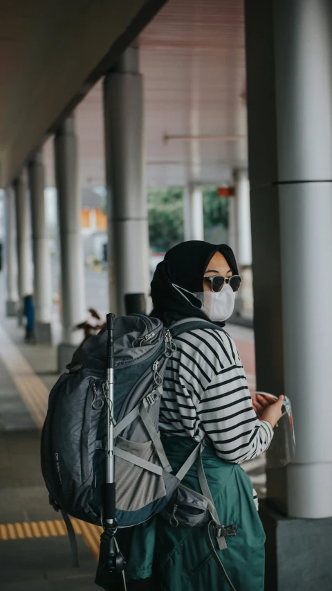 a woman with a mask and backpack looks at her phone