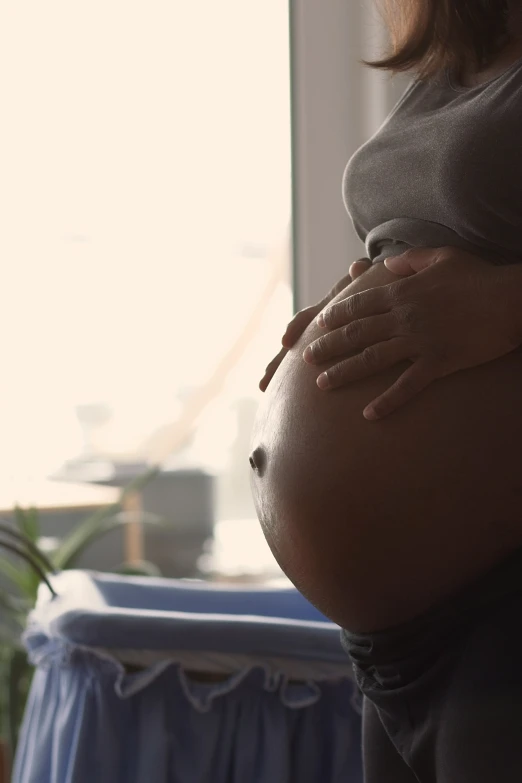 a pregnant belly is visible against a window sill