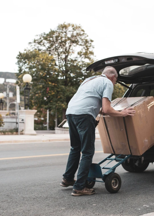 an old man is putting the cardboard into the back of a vehicle