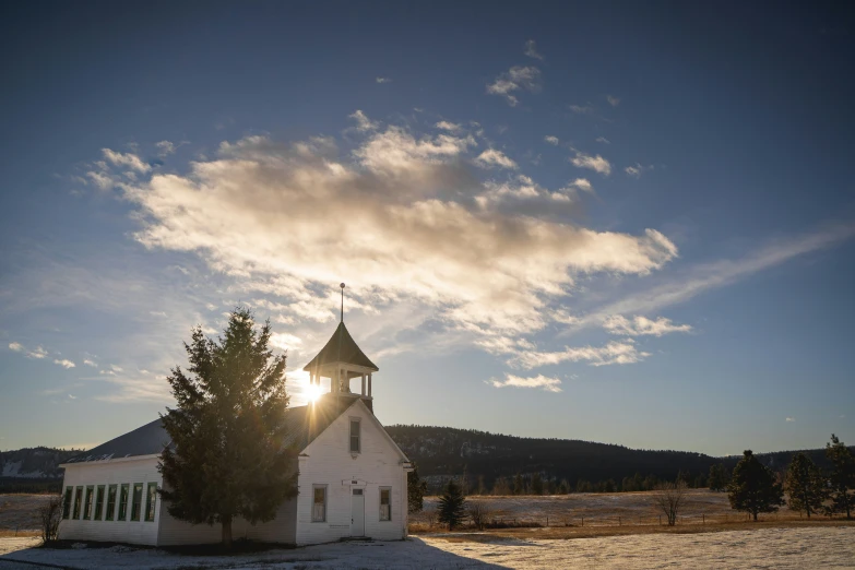 the sun peeks over a small church in a winter field