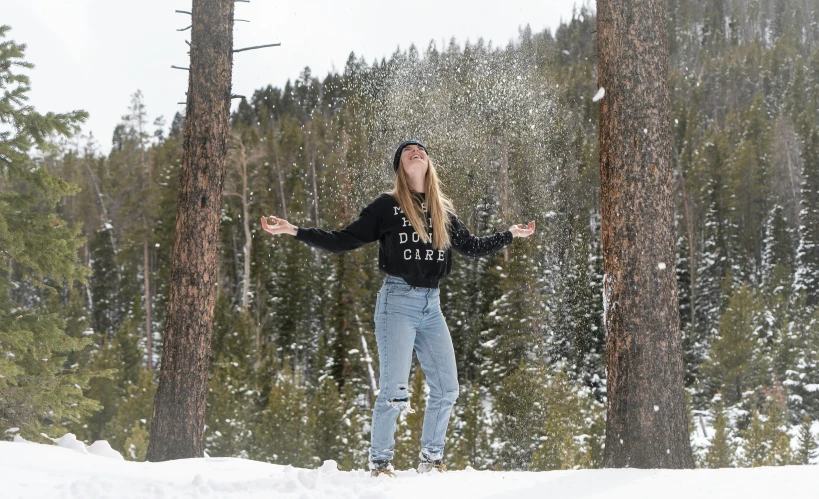 a woman standing on a snowboard surrounded by trees