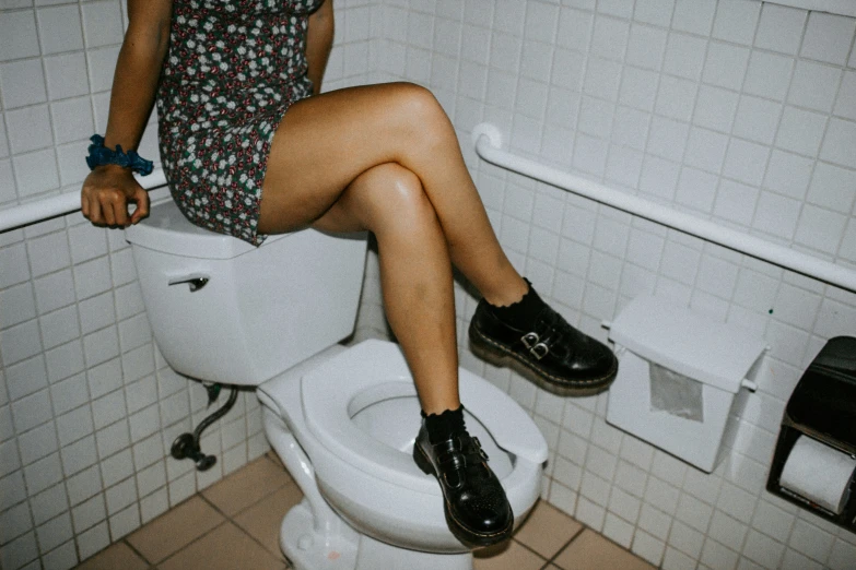 a girl in black boots and a floral dress sitting on a toilet