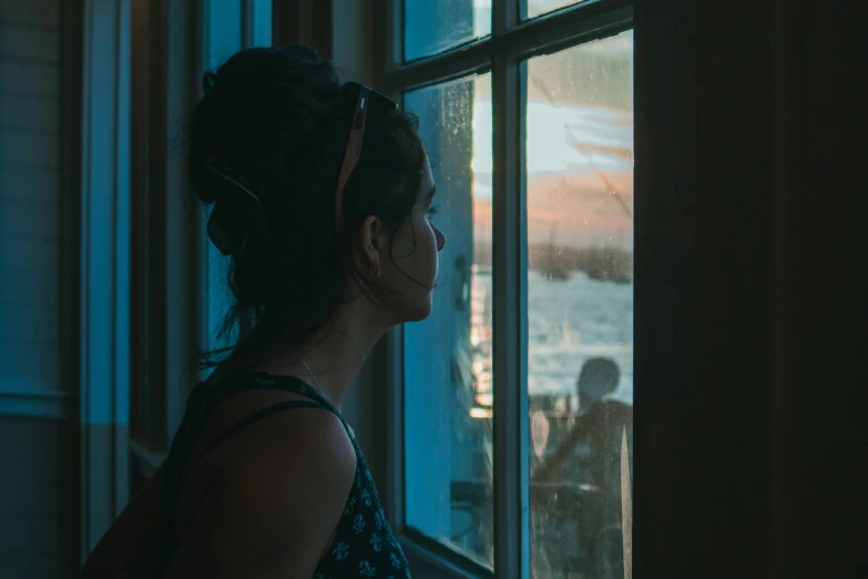 a woman standing by a window in the dark looking at a snow capped mountain