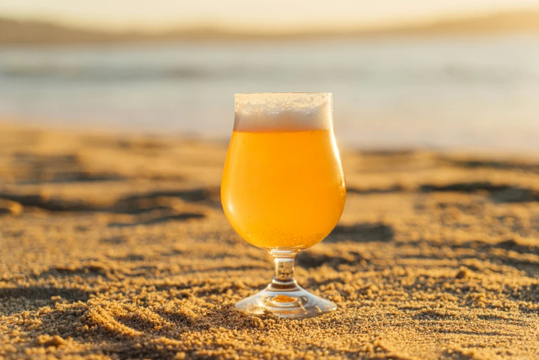 a glass filled with liquid sitting in the sand