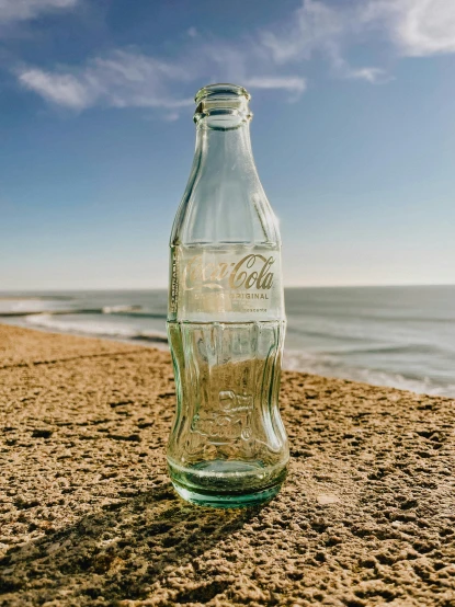an empty glass bottle sitting on top of a sandy beach
