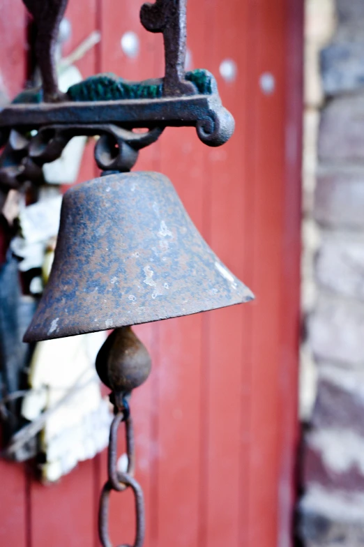 a rusted bell hanging on the side of a red door