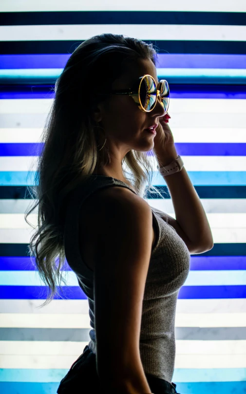 a young woman standing in front of a striped wall with large sunglasses