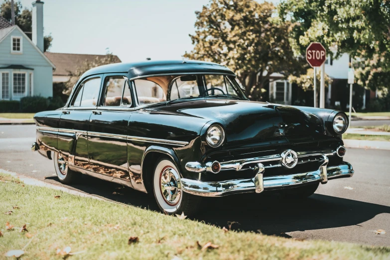 an old black car on the street with houses in the background