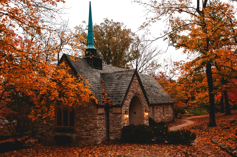 a small building with a spire is surrounded by fall colored trees