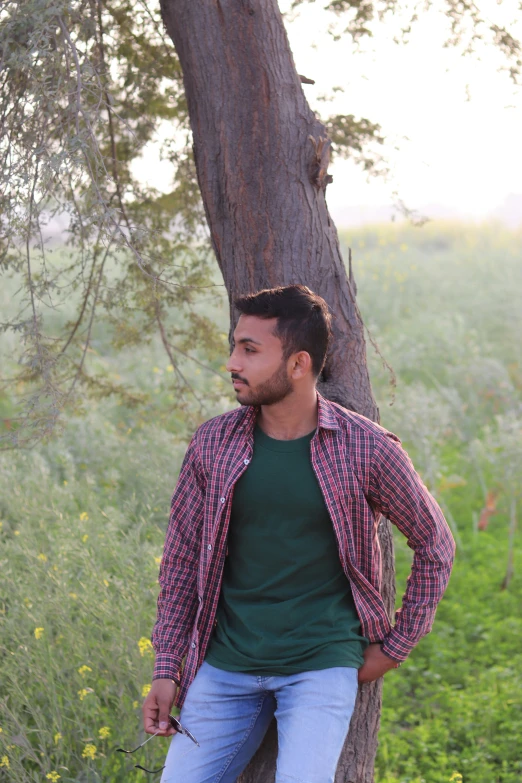 a man in plaid jacket leaning against a tree