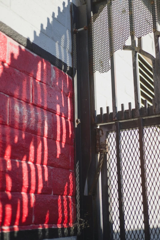 a red wall behind an iron gate with the shadow cast onto it