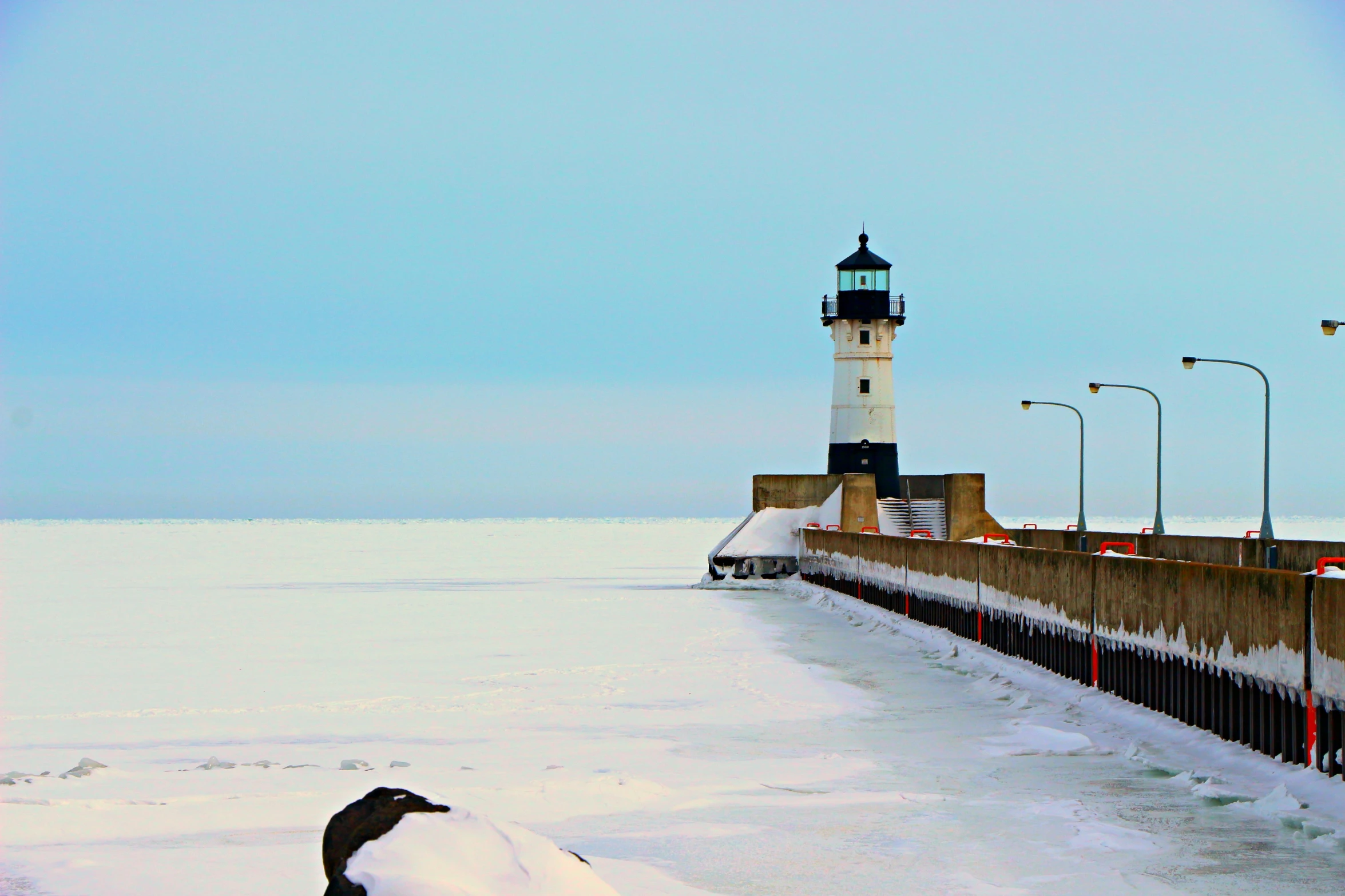 a lighthouse stands on the shore of a frozen lake