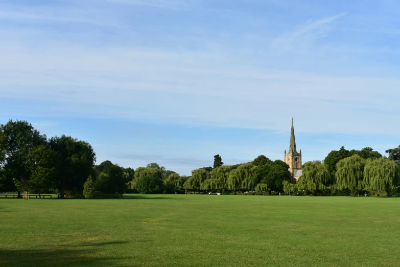 a large field in the middle of a park with a church in the distance