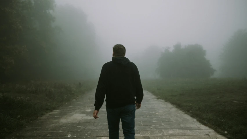 man walking down a path with an umbrella in the fog