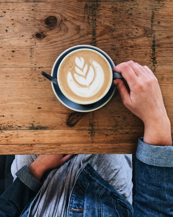 a person holding a mug of coffee on top of a wooden table