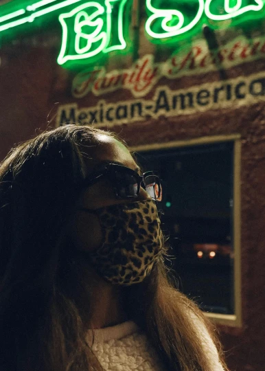 a woman standing outside a mexican restaurant wearing a scarf and shades