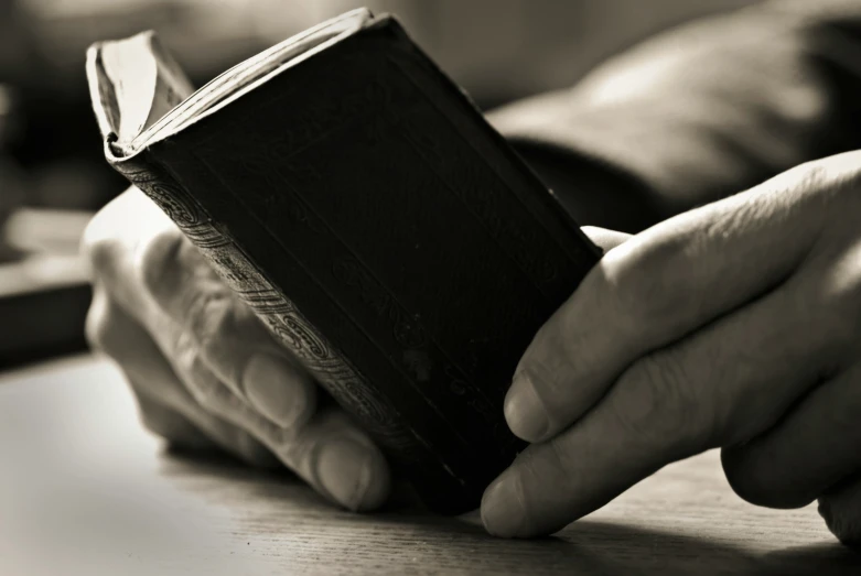 two hands holding a small book in the middle of the image