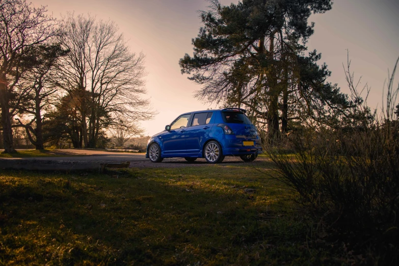 a blue compact vehicle is parked on the side of the road in front of some trees