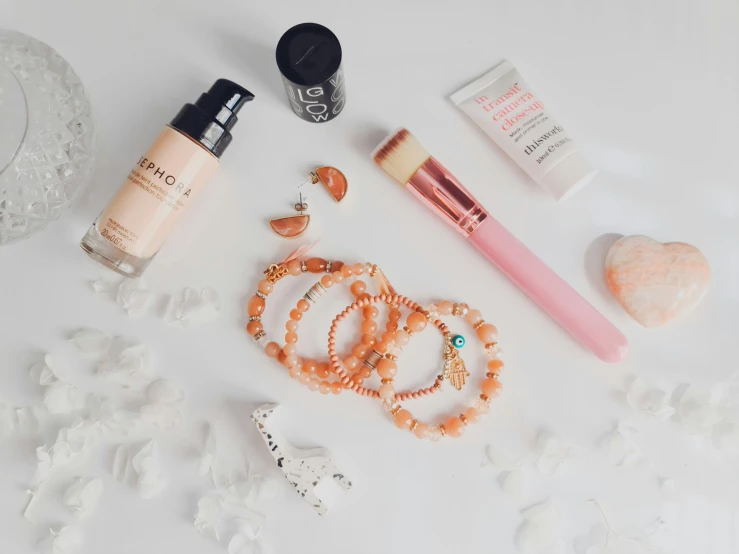 some cosmetics, a necklace and jewelry are on a white surface