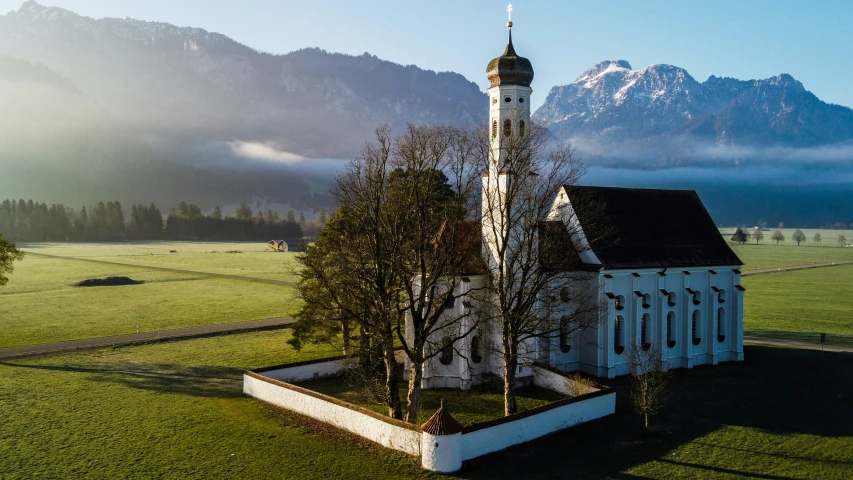 a church in a green field with mountains in the distance