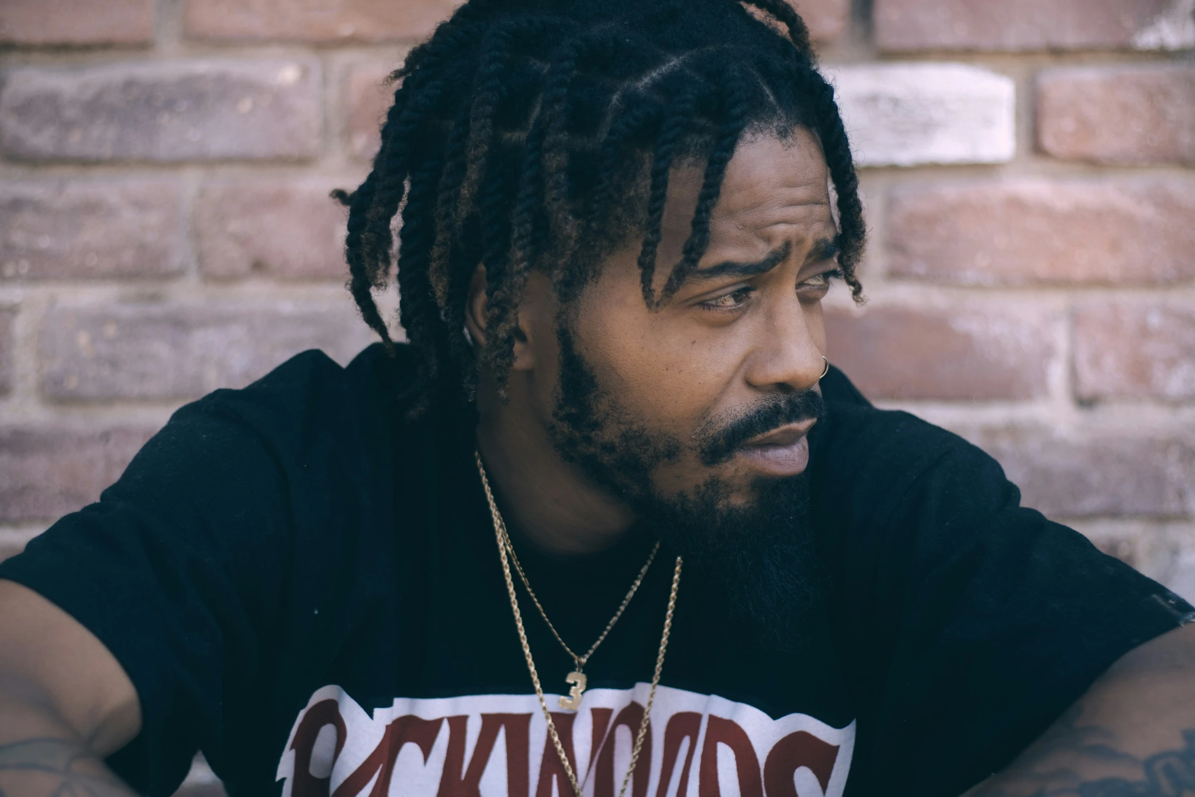 a man with dreadlocks and black shirt next to brick wall