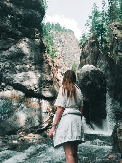a woman is walking down the rocks next to a waterfall