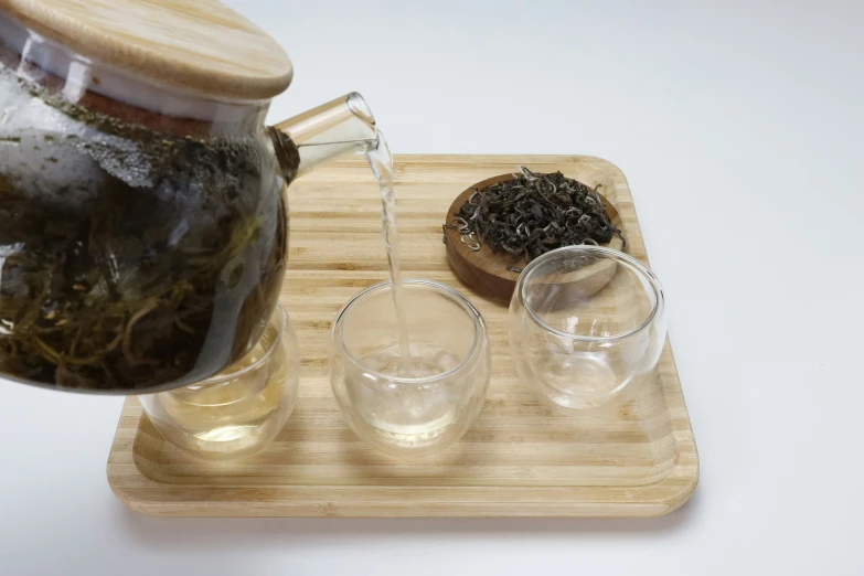 tea being poured into clear glass on wood tray