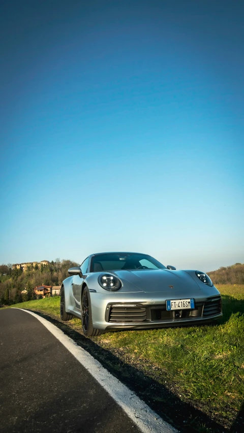 a large silver car is parked on the grass by a road