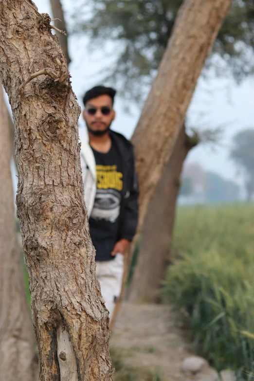 a man wearing sunglasses standing behind some trees