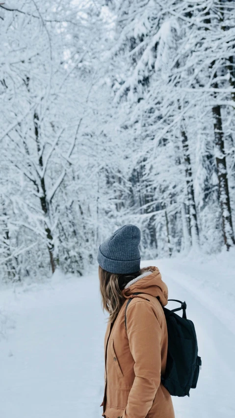 woman walking in the snow in an all - brown outfit and hat