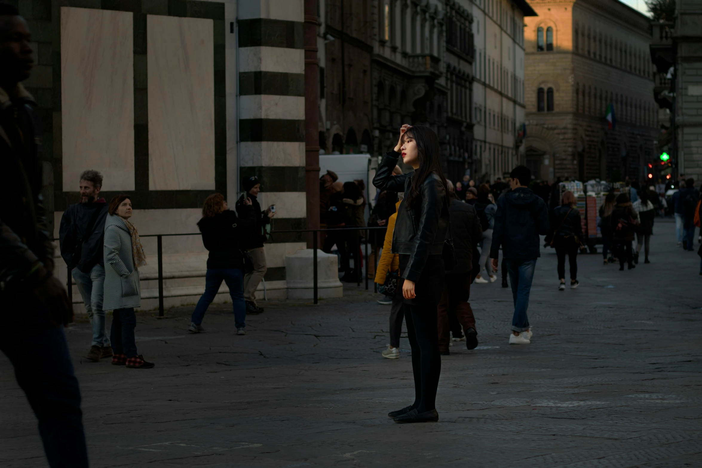 man standing alone talking on his cellphone while others walk along the street