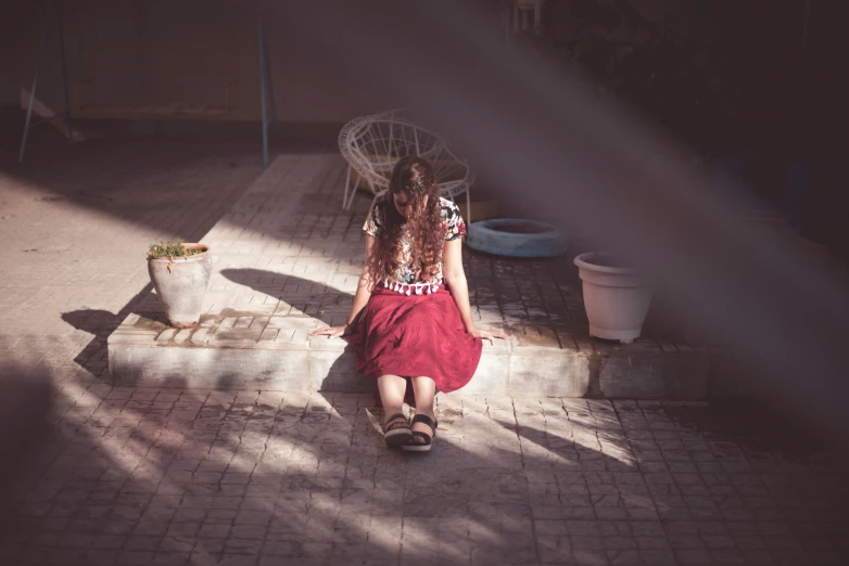 the woman sits in the middle of the walkway, outside with an umbrella