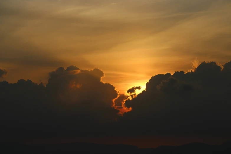 the sun setting behind clouds, with a plane flying in the foreground