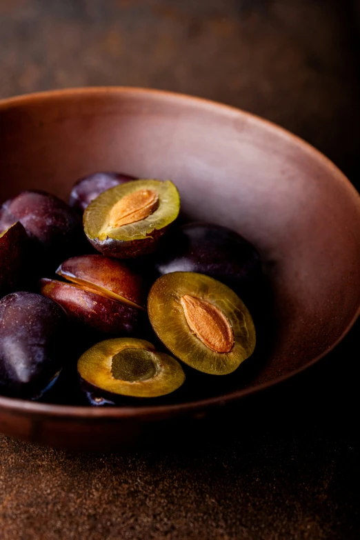 a bowl of peeled plums sits on a brown surface