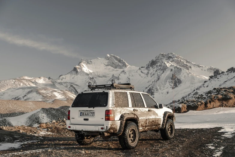 an suv is parked in the snow on the ground near a mountain range