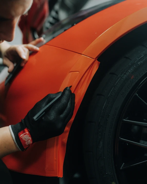 a person is putting on gloves on an orange car