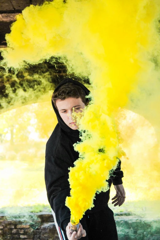 the man is wearing a hooded jacket and holding a stick, with colored smoke coming out of his face