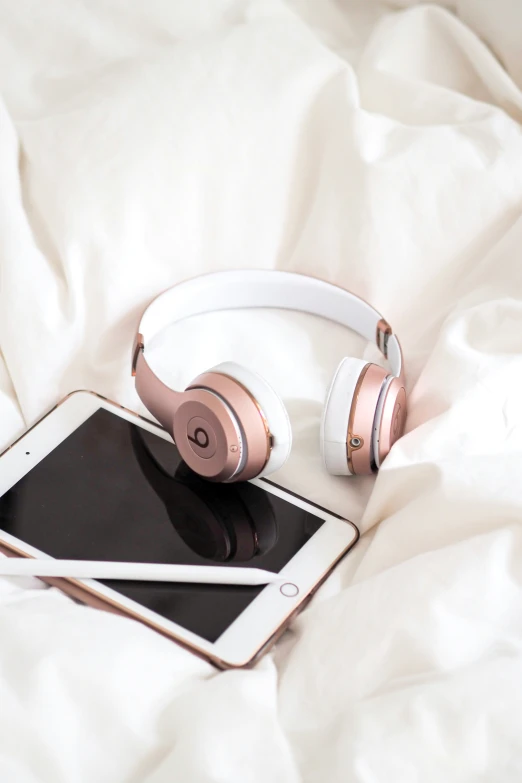 headphones and tablet on a white bed with sheet