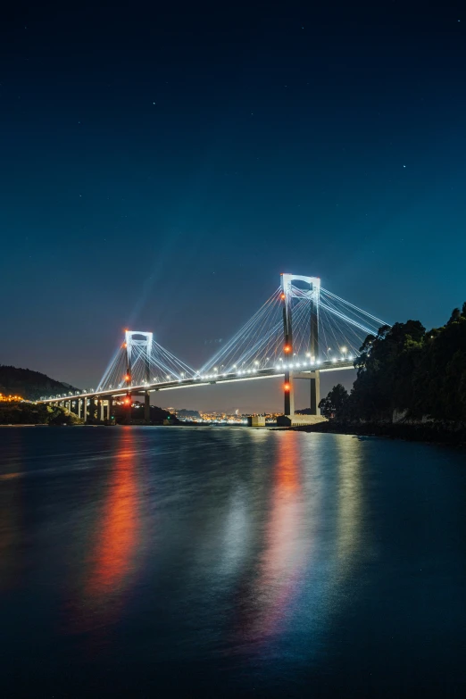 a view of a large bridge with water and night lights