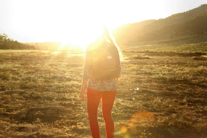 a young person stands on the edge of a grassy area in front of a sun flare