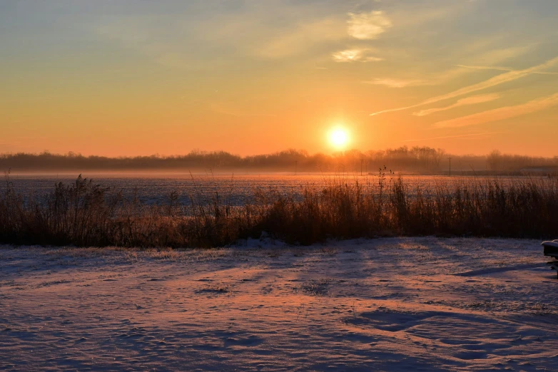 the sun sets behind a field covered with snow