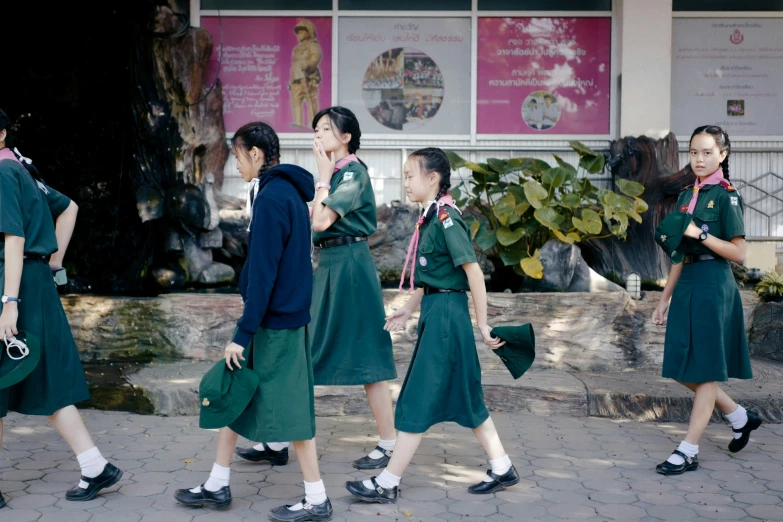 four girls walking across a pavement in green dress