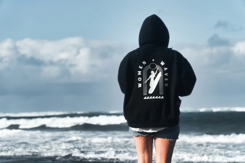 a woman standing on the beach in a sweatshirt