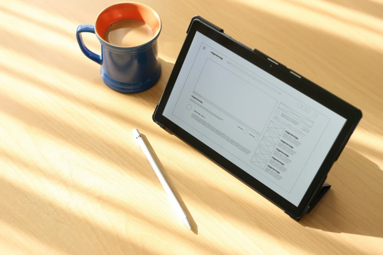 an ipad and cup sitting on a table with a pen