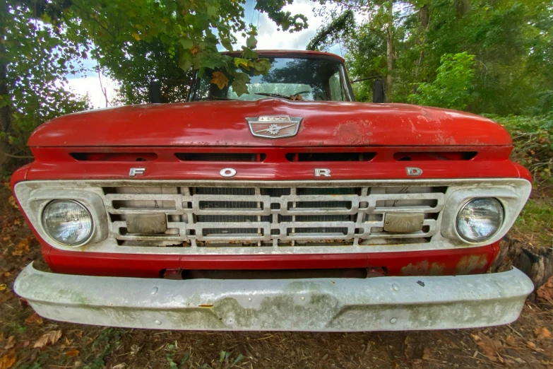 an old, rusty red truck parked in the woods