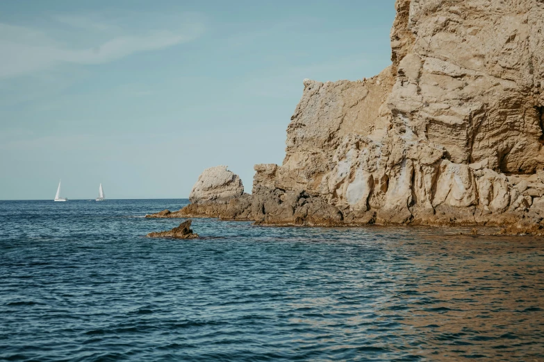 three sailboats in the sea near a rock formation