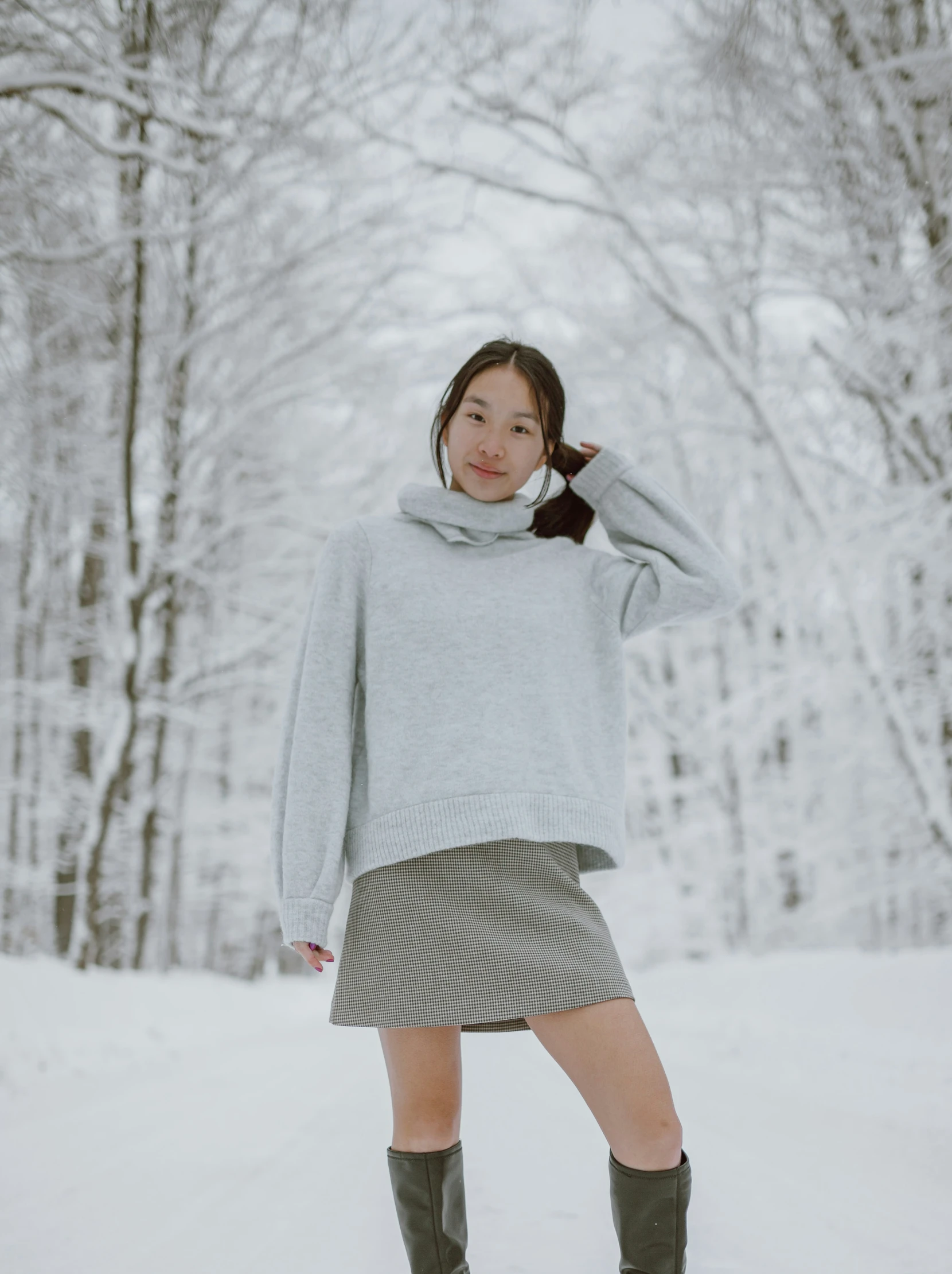 a young woman standing in the snow wearing boots and a sweater