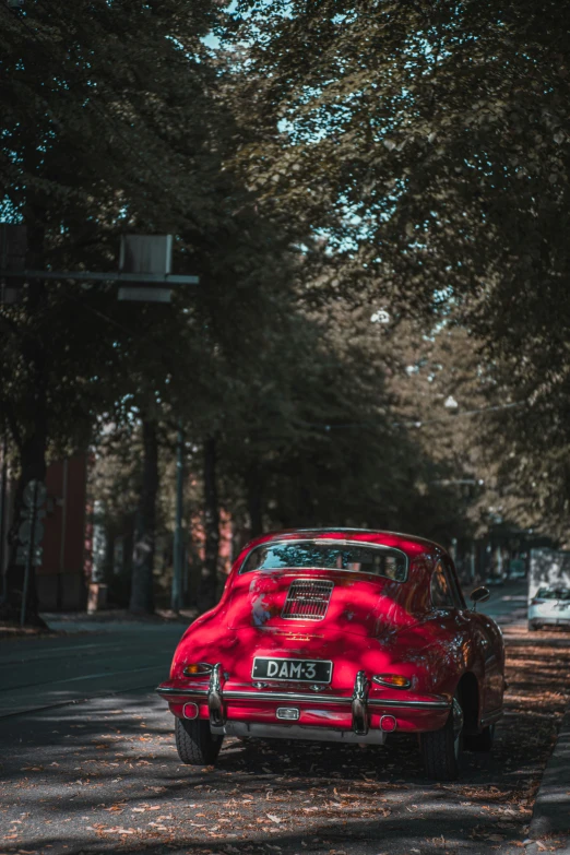 an old car is parked on the road in front of a row of trees